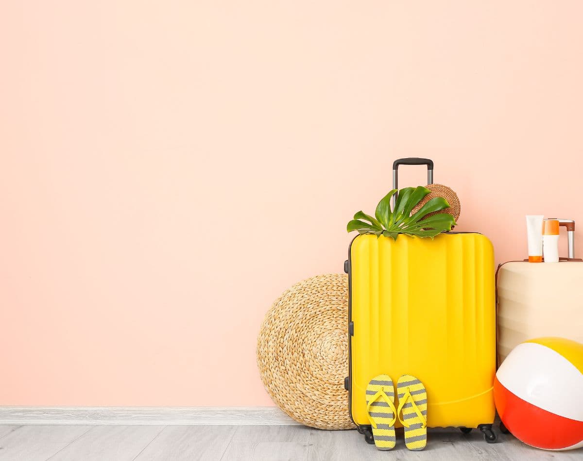 yellow suitcase with beach vacation items like flip-flops, beach hat and sunscreen.