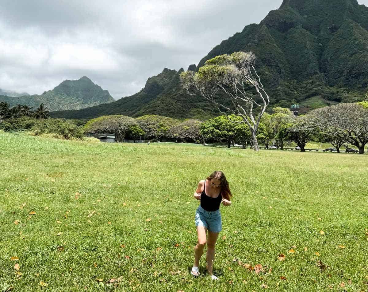 a girl standing with a stunning background of mountains in kualoa ranch.