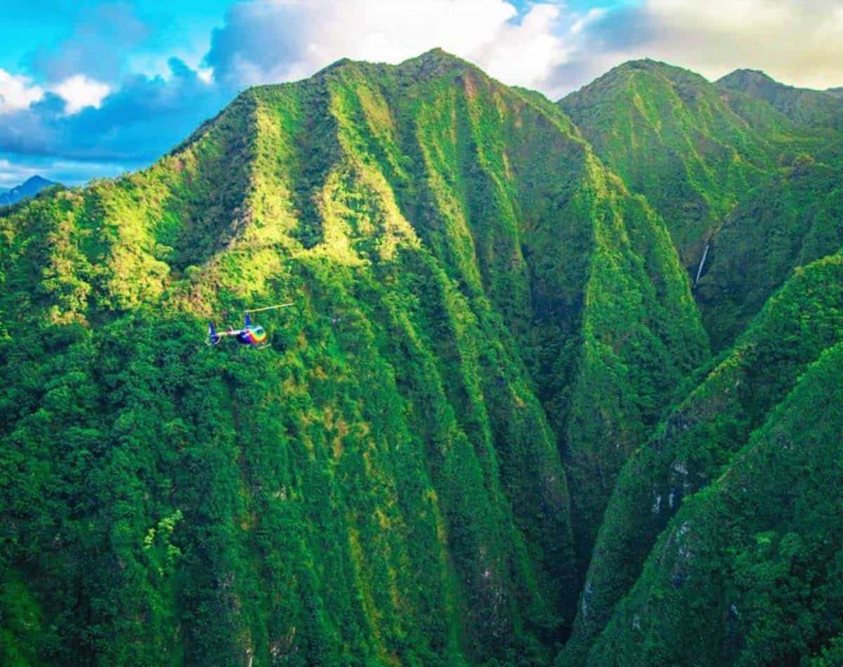 helicopter flying over the green mountains in oahu, hawaii.