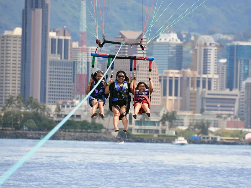 a group of 3 people parasailing with waikiki beach backdrop.