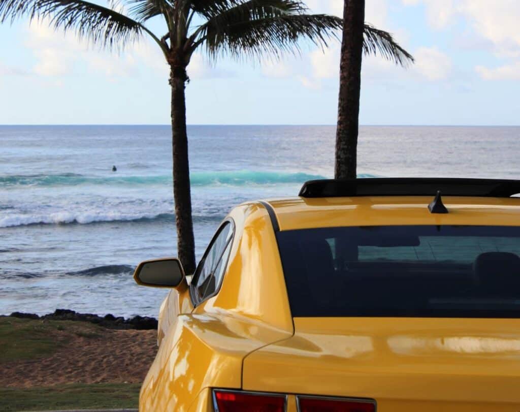 yellow cab with palm trees and ocean backdrop in oahu, hawaii.