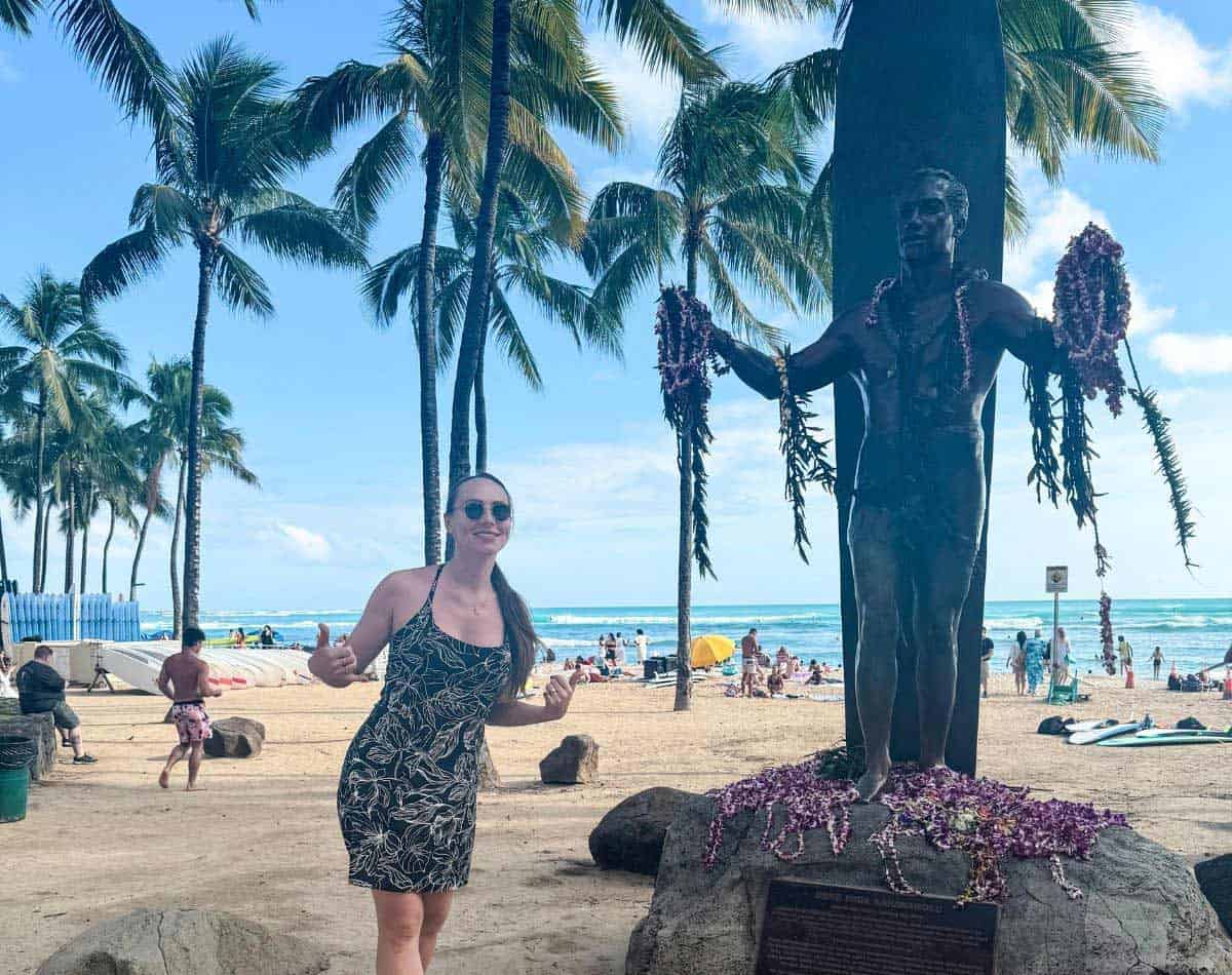 a girl standing in front of statue in waikiki beach.